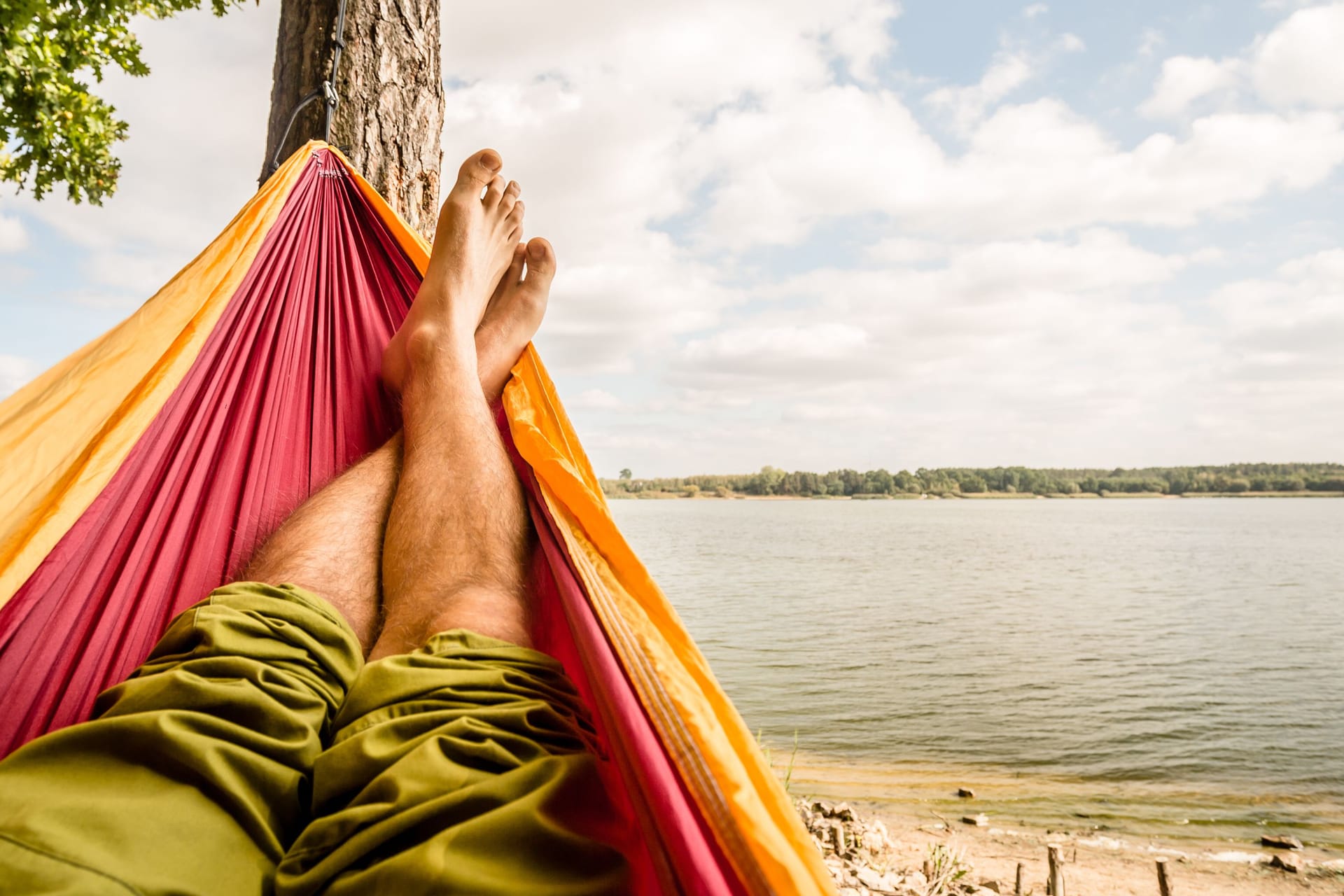 Relaxing in the hammock at the beach under a tree, summer day. Barefoot man laying in hammock, looking on a lake, inspiring landscape Relaxing in the hammock at the beach under a tree, summer day. Barefoot man laying in hammock, looking on a lake, inspiring landscape
