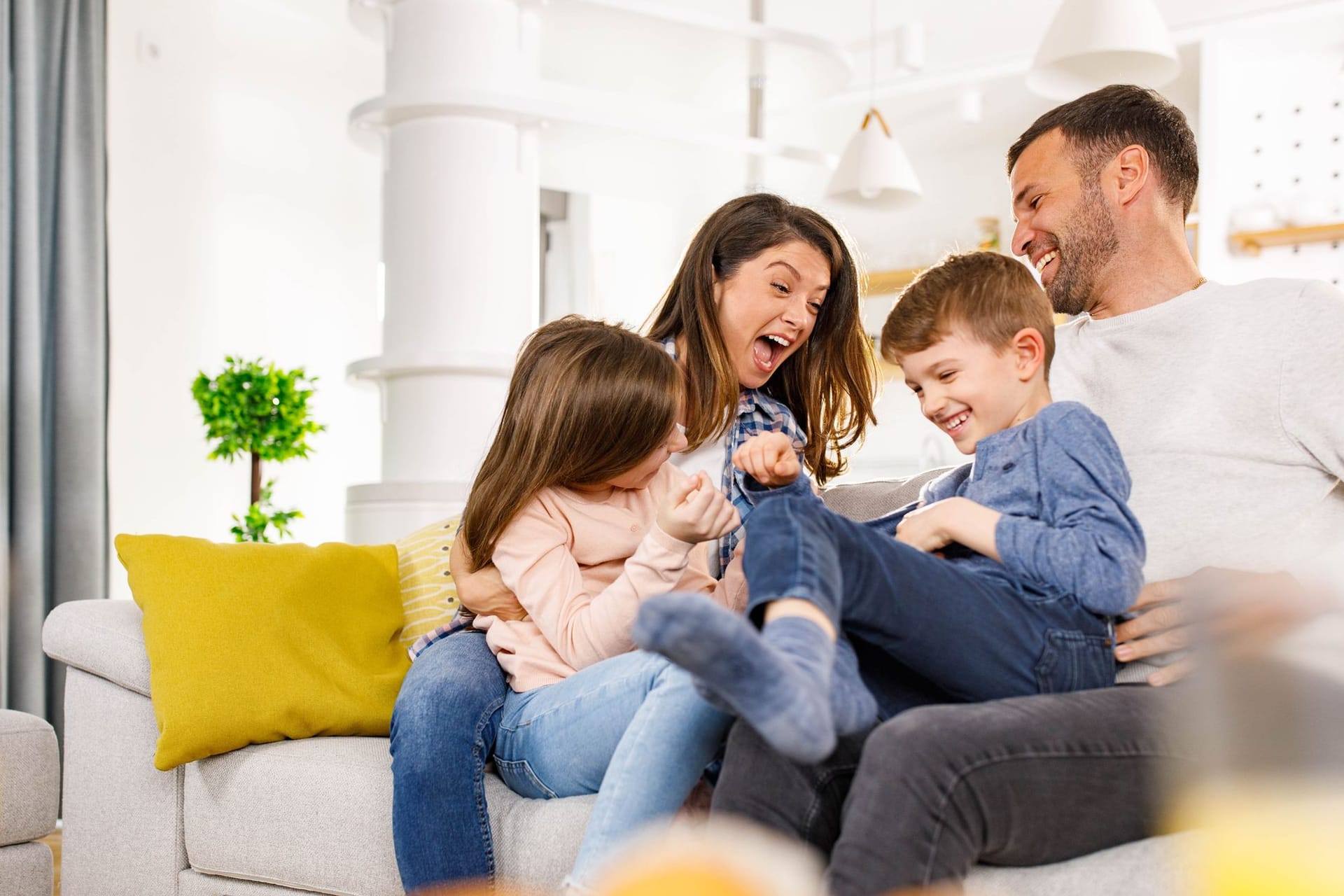 Familie mit zwei Kindern sitzt fröhlich auf dem Sofa Familie mit zwei Kindern sitzt fröhlich auf dem Sofa
